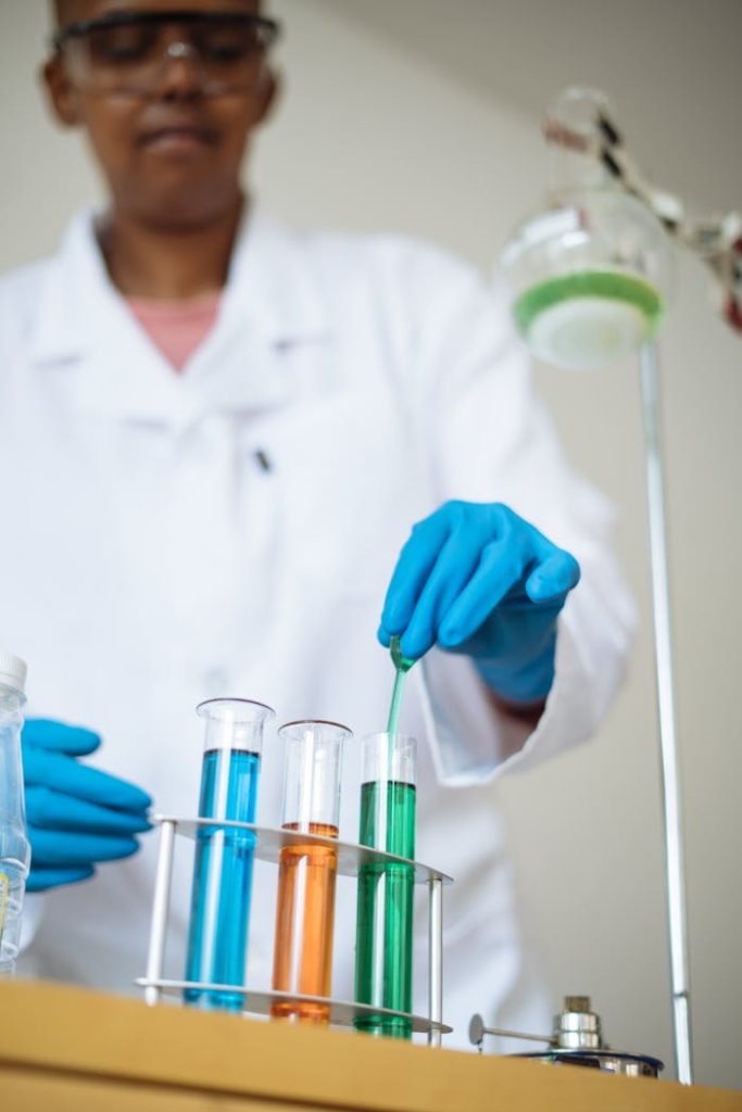 Focused African American student in safety glasses and uniform investigating chemical reactions while collecting sample with pipette from test tube during chemistry lesson